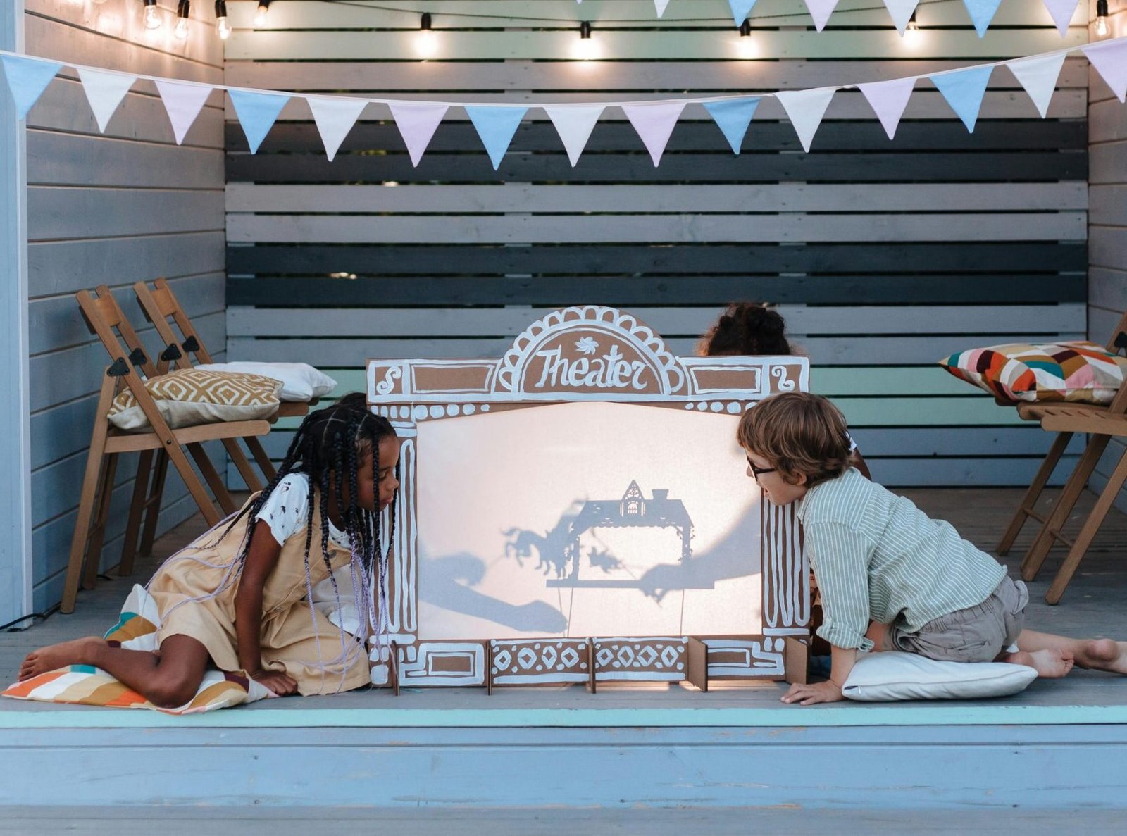 Children engage in creative puppet play at an indoor shadow theater with festive decorations.